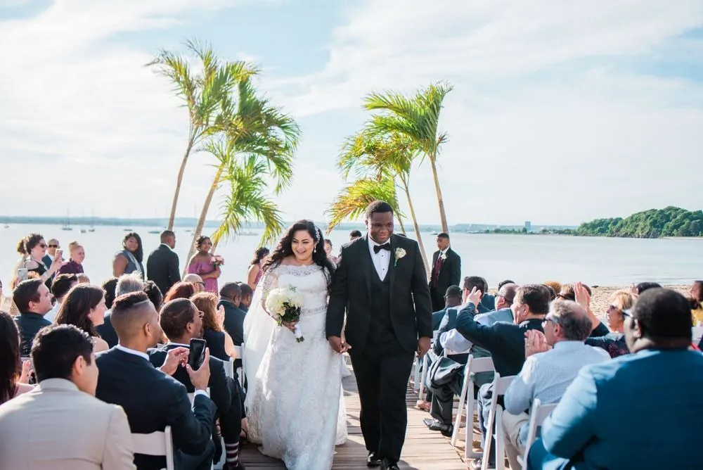 Natasha and Jordan walk back up the boardwalk aisle as guests cheer under palm trees