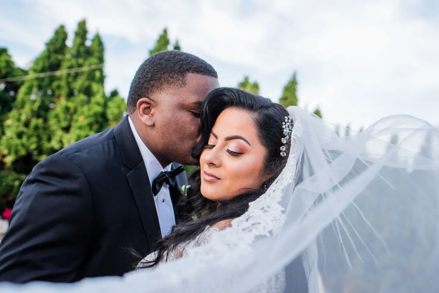 Jordan presses his cheek to Natasha's as her lace veil blows across them both