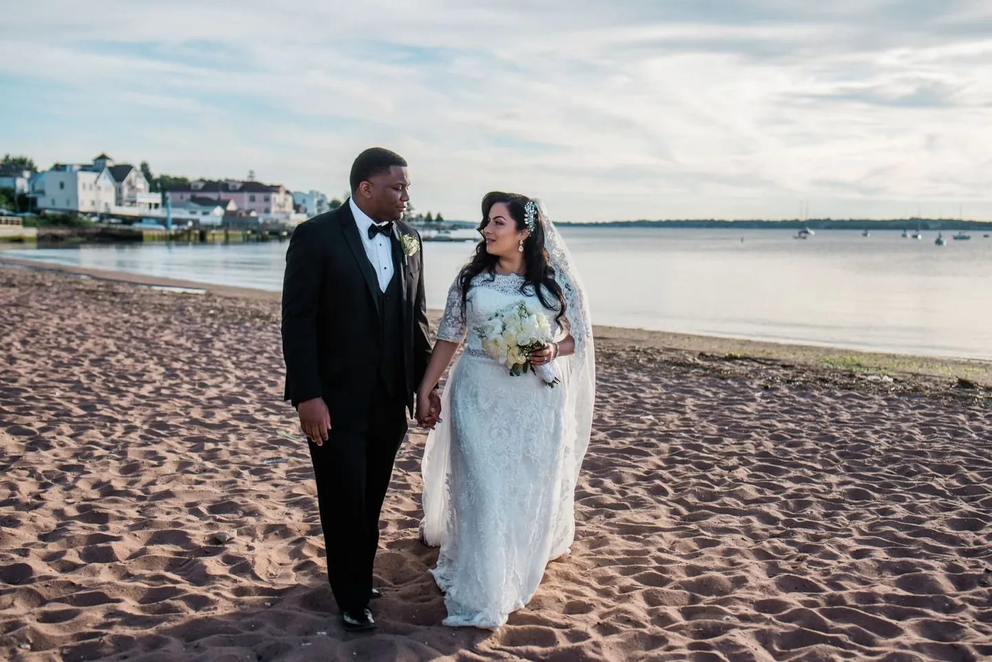 Natasha and Jordan walk arm in arm along the beach toward the camera in evening light