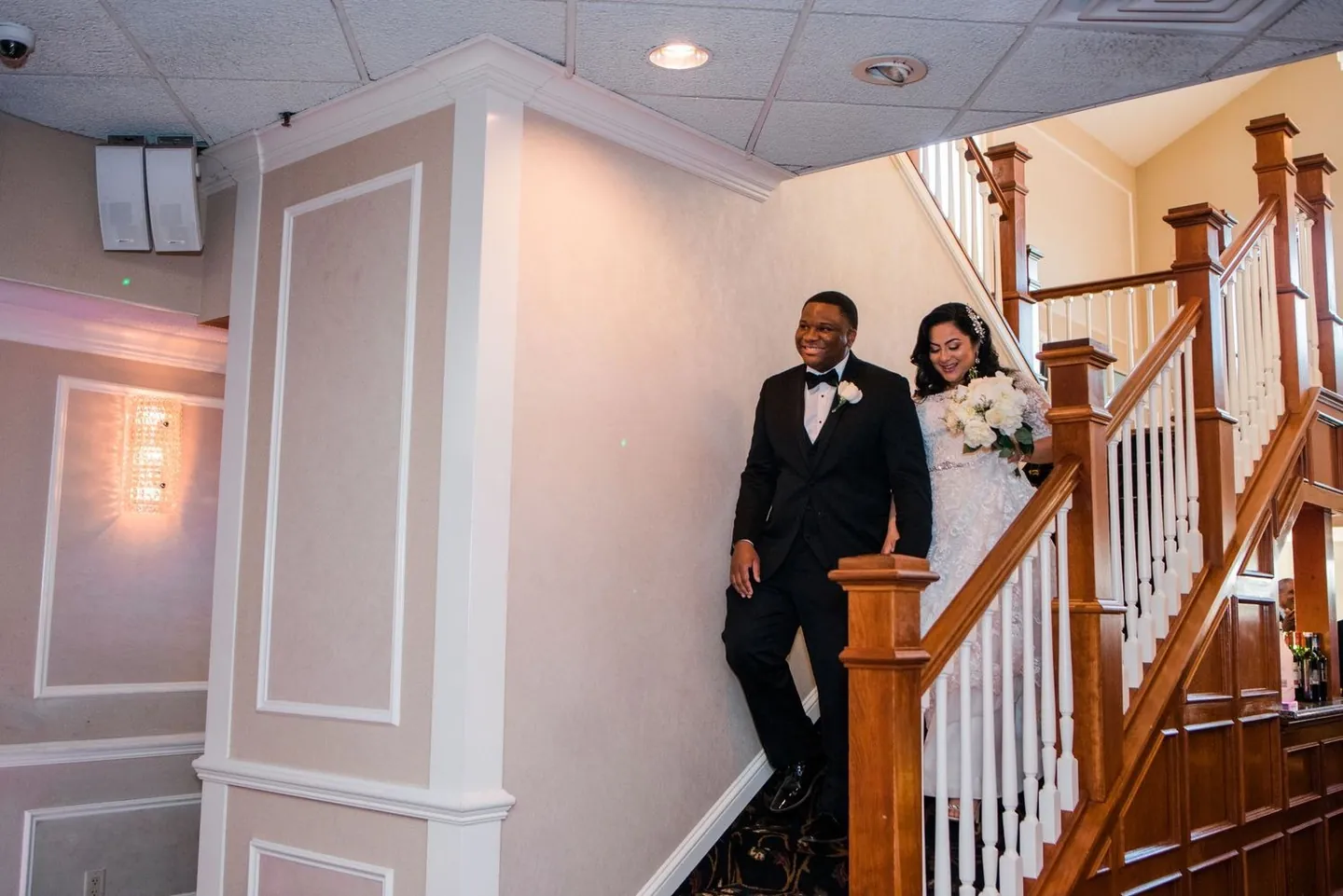 Natasha and Jordan come down a curved wooden staircase into the reception