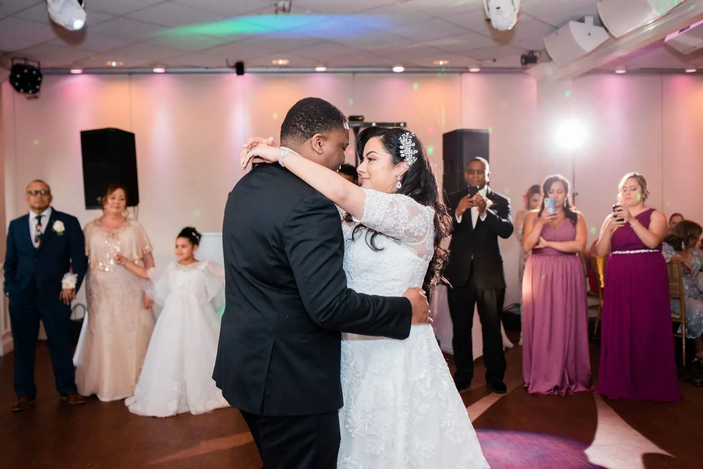 First dance under pink uplighting as bridesmaids in plum watch from the edge