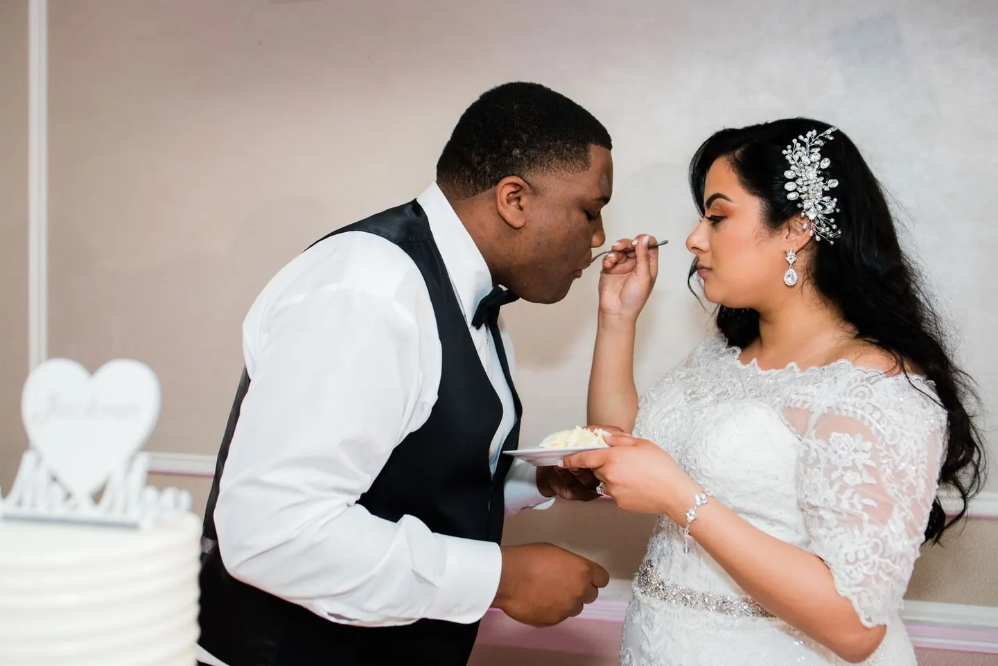 Natasha feeds Jordan a bite of cake beside the white tiered cake