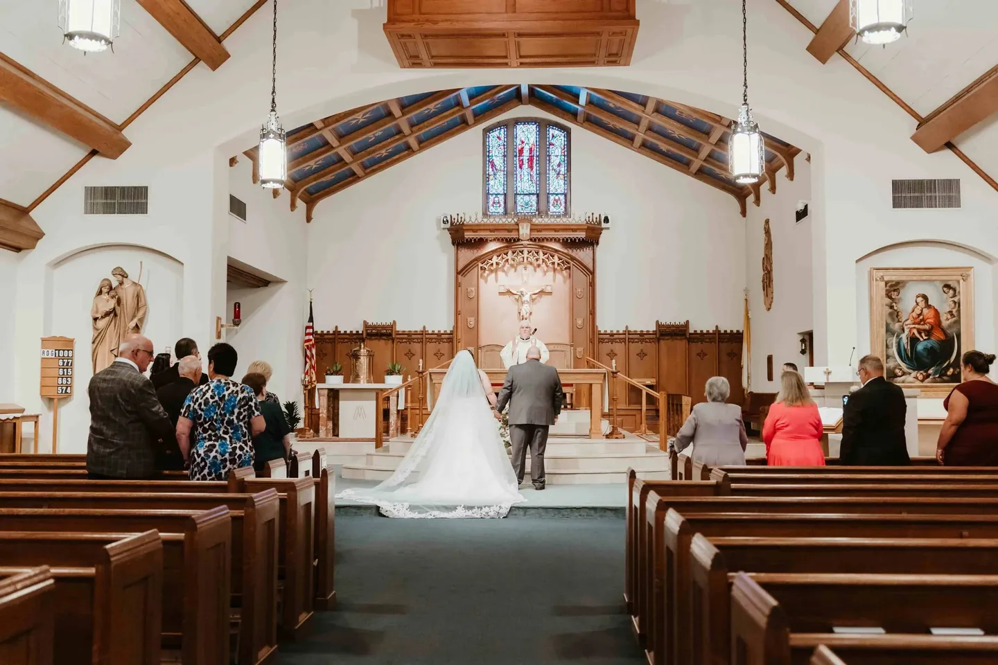 Nicole and Ryan stand at the altar before the priest as a few family members watch from the pews