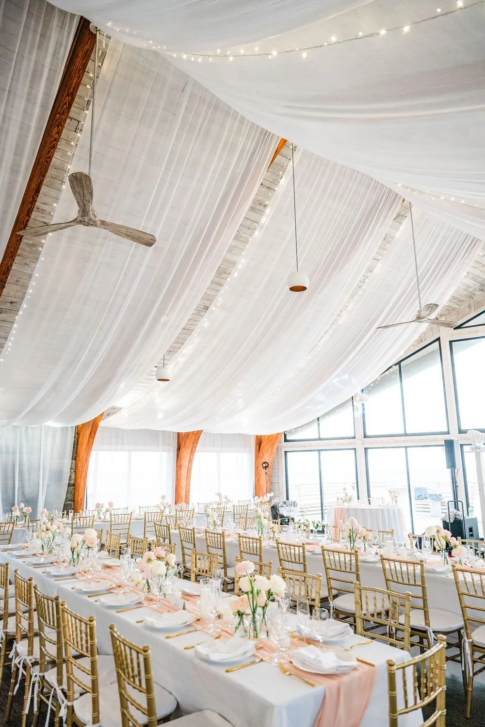 Long reception tables under white draped ceiling fabric inside the pavilion, windows facing the beach