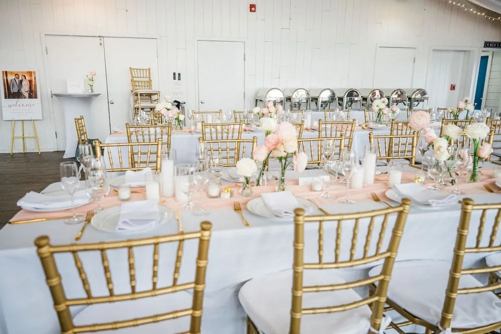 Gold chiavari chairs, blush runners, and white candles set along reception tables in the pavilion