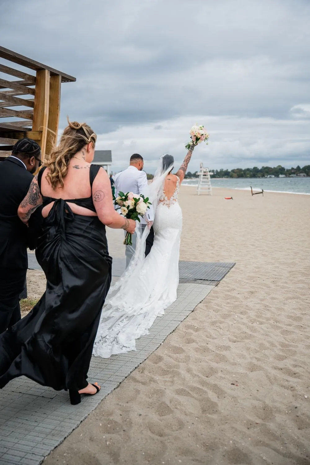 Olivia throws her bouquet arm in the air walking back up the aisle on the sand