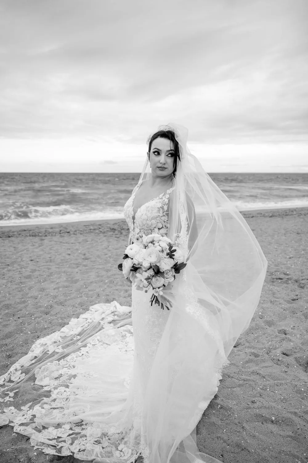 Black and white portrait of the bride with her veil sweeping across the sand behind her