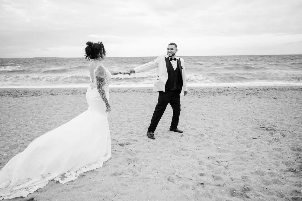 Black and white frame of Elvin leading Olivia by the hand along the water's edge
