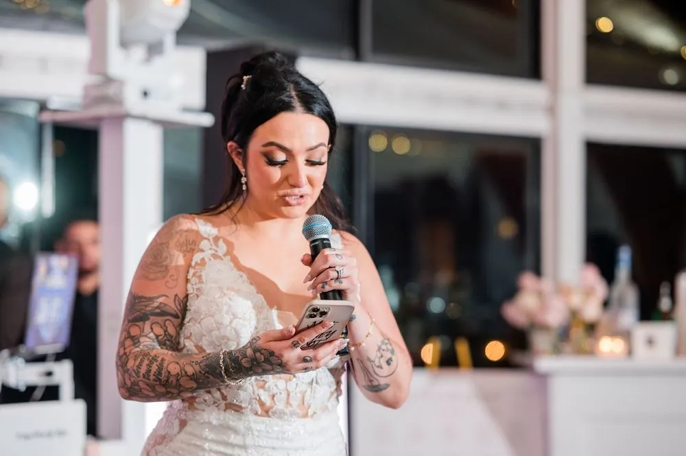 Bride reads her toast from her phone into a microphone inside the candlelit pavilion