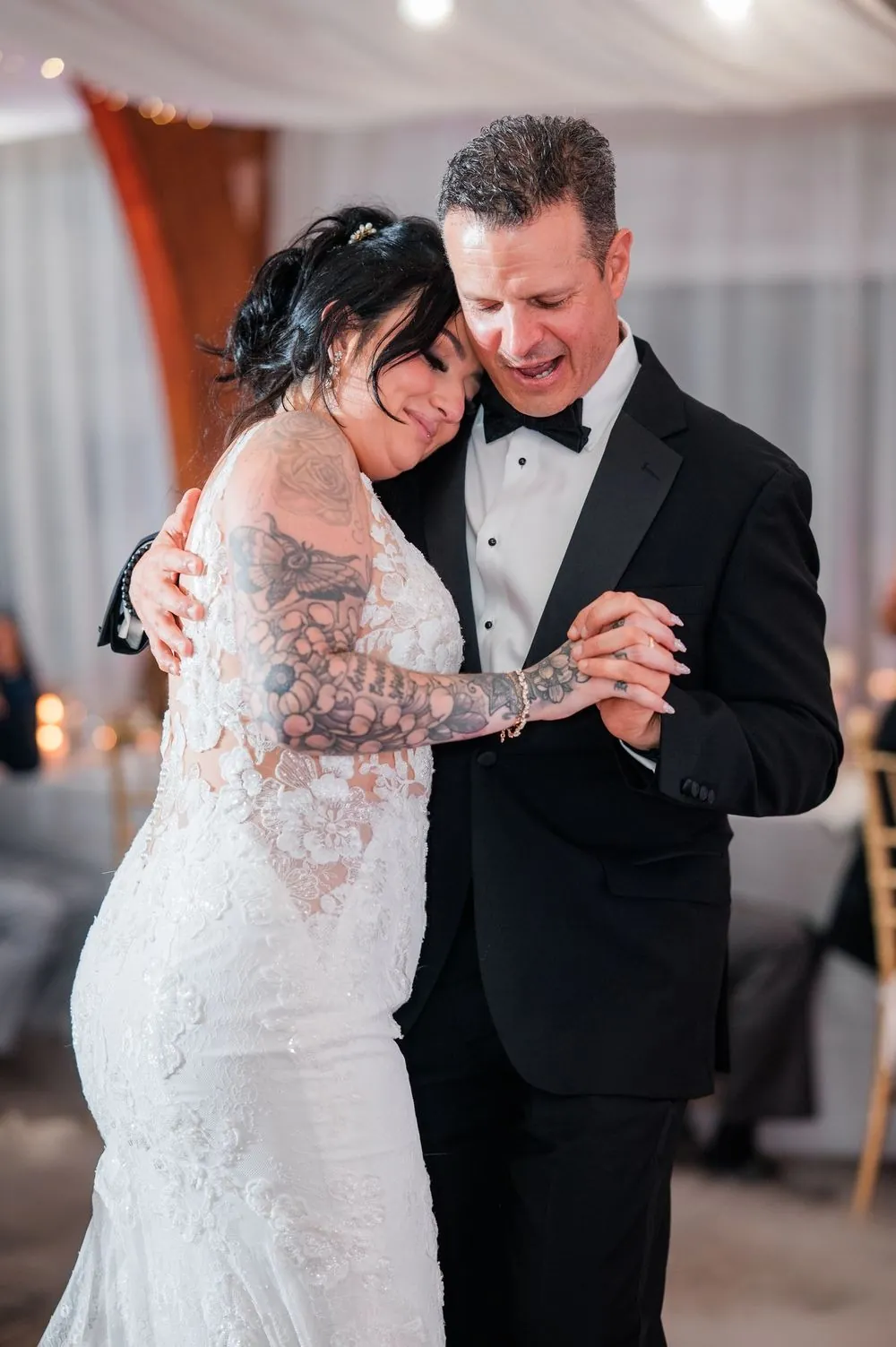 Bride rests her head on the shoulder of a man in a black tuxedo during a slow dance