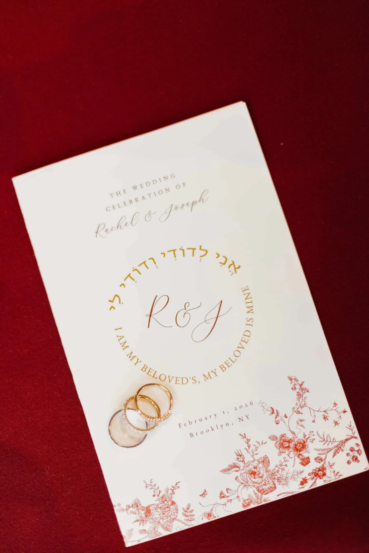 A wedding program in gold ink with Hebrew lettering and 2 gold rings on red velvet