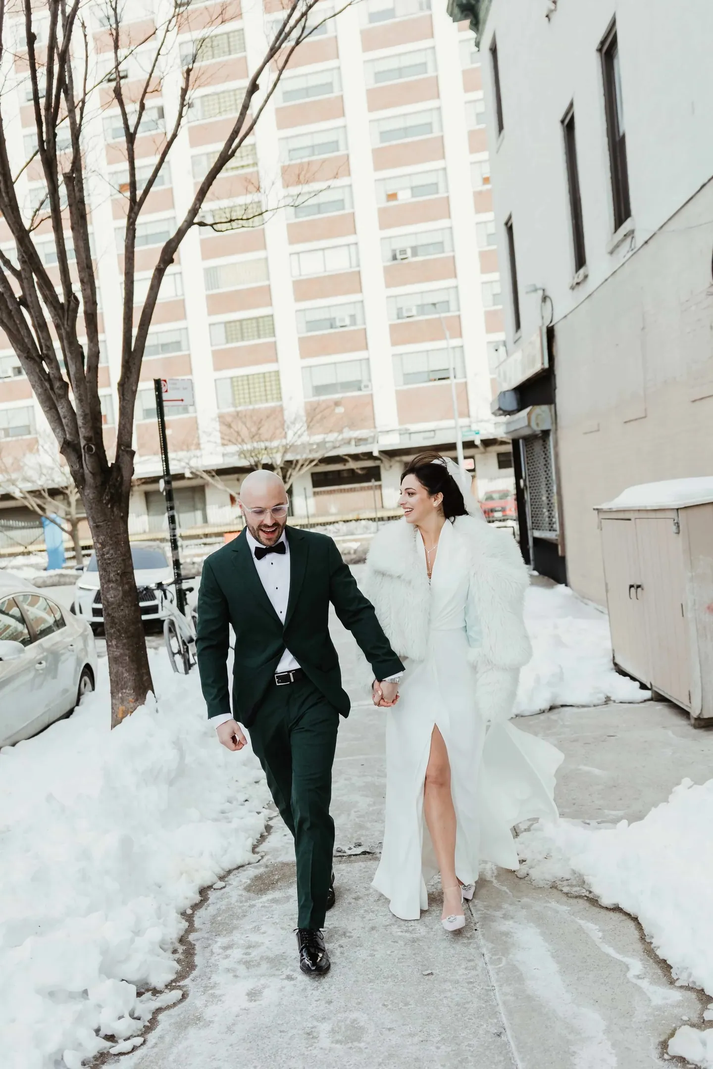 Rachel and Joe walk hand in hand past snowbanks and bare trees