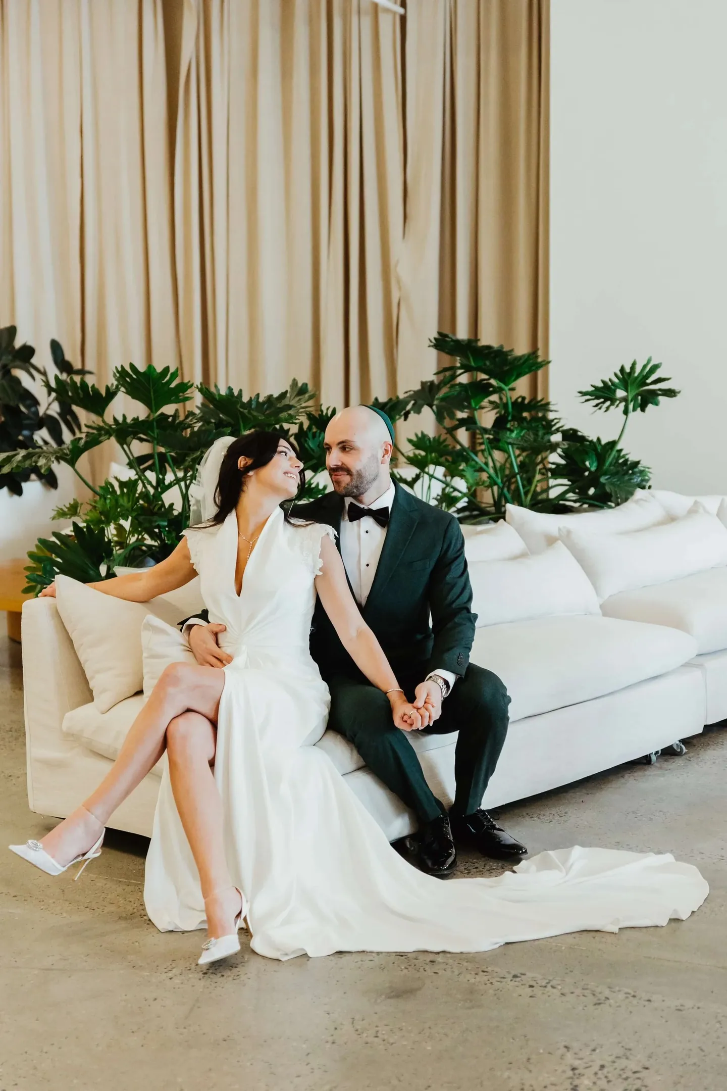 Rachel and Joe sit together on a white sofa beneath tall windows