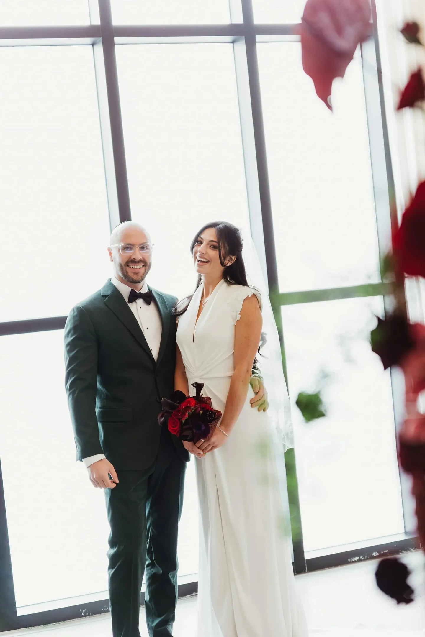 Rachel and Joe stand side by side in front of a wall of steel-framed windows