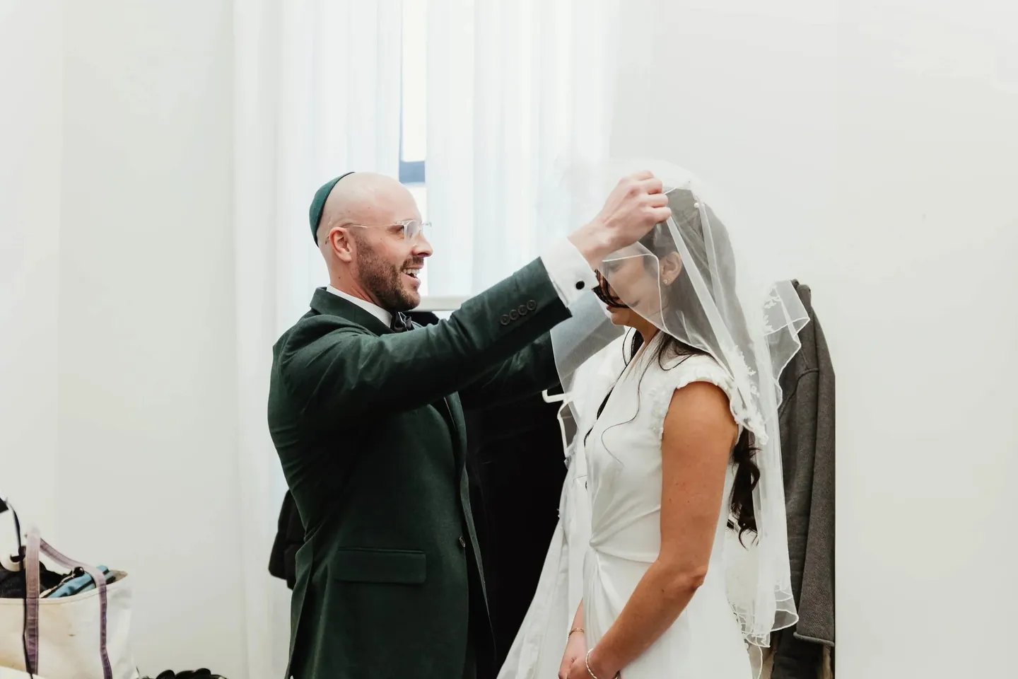 The groom lowers the veil over the bride's face as both of them laugh