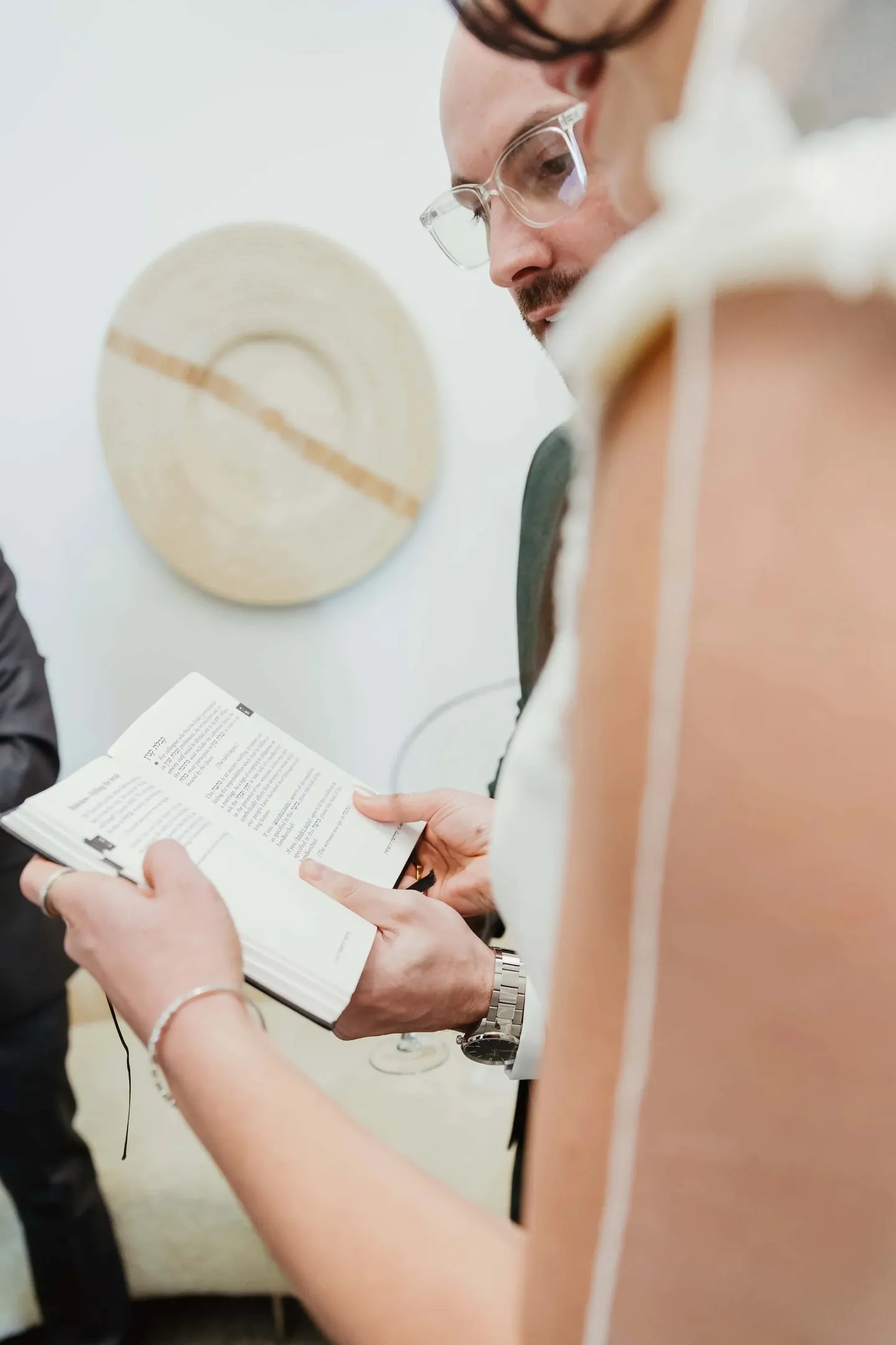 A man in glasses reads from a small booklet beside the bride's veil