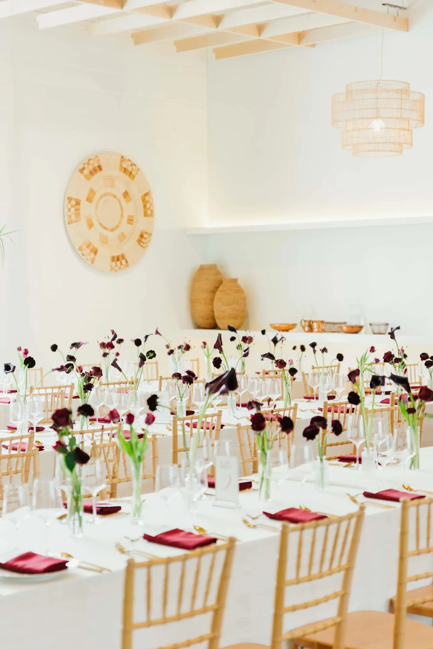 Long tables with gold chairs and burgundy stems fill a white reception room