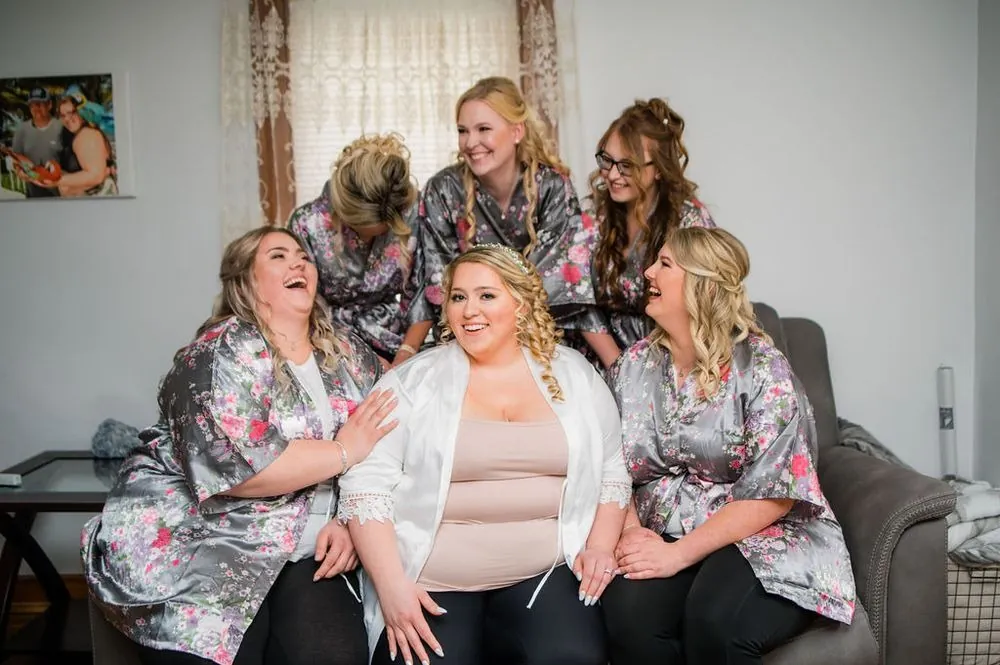 The bride laughs on a sofa with bridesmaids in matching floral robes
