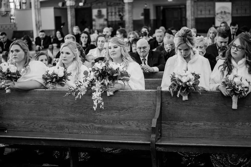 Bridesmaids rest their bouquets on the pew in front of them during the service, in black and white