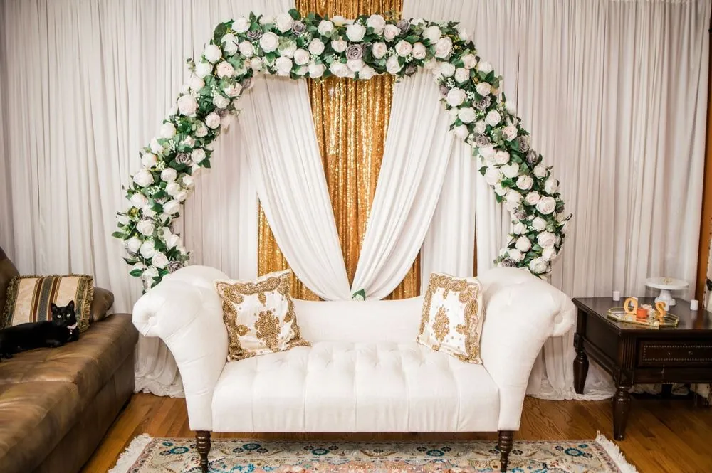 A white tufted settee under an arch of white and gray roses in the living room
