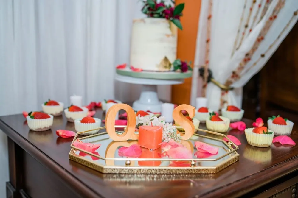A dessert table with wooden Q and S letters, strawberry cups and scattered rose petals