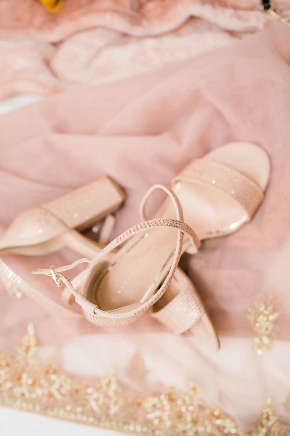 Blush embroidered shoes resting on folded pink fabric with gold trim