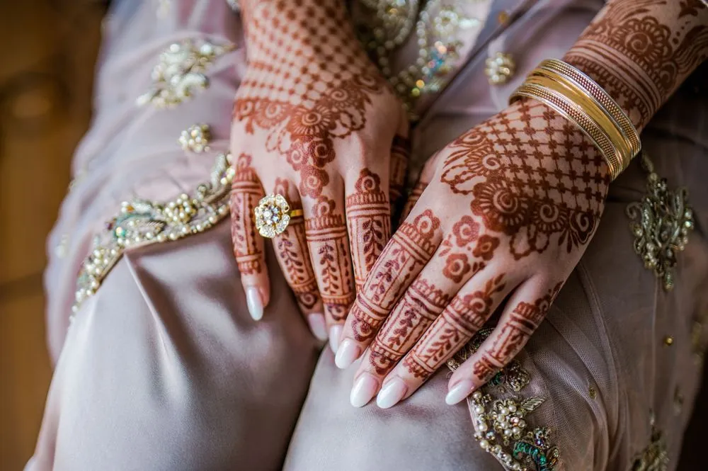 The bride's hands covered in detailed henna rest on her blush and gold gown