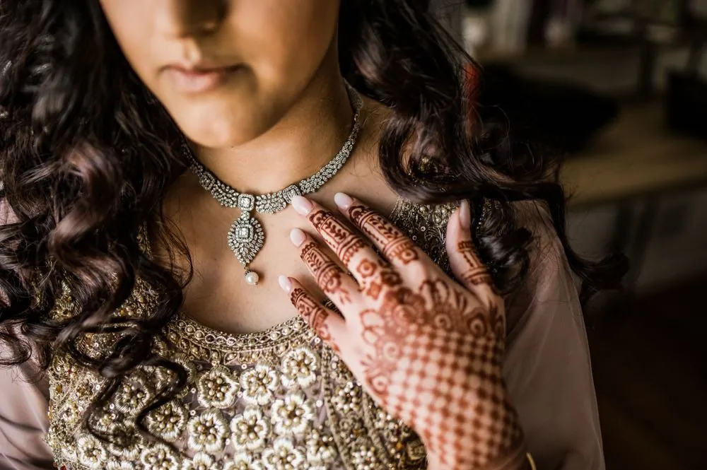Close view of the bride's henna-covered hands touching a diamond necklace