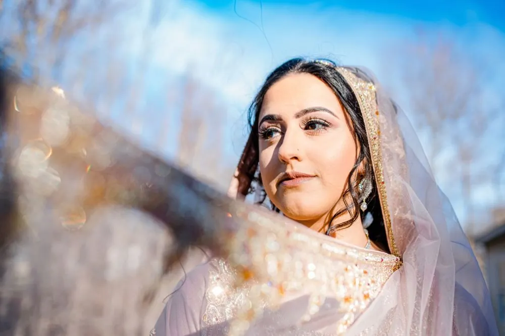 The bride looks up into a bright blue sky, her sheer dupatta lifting in the breeze