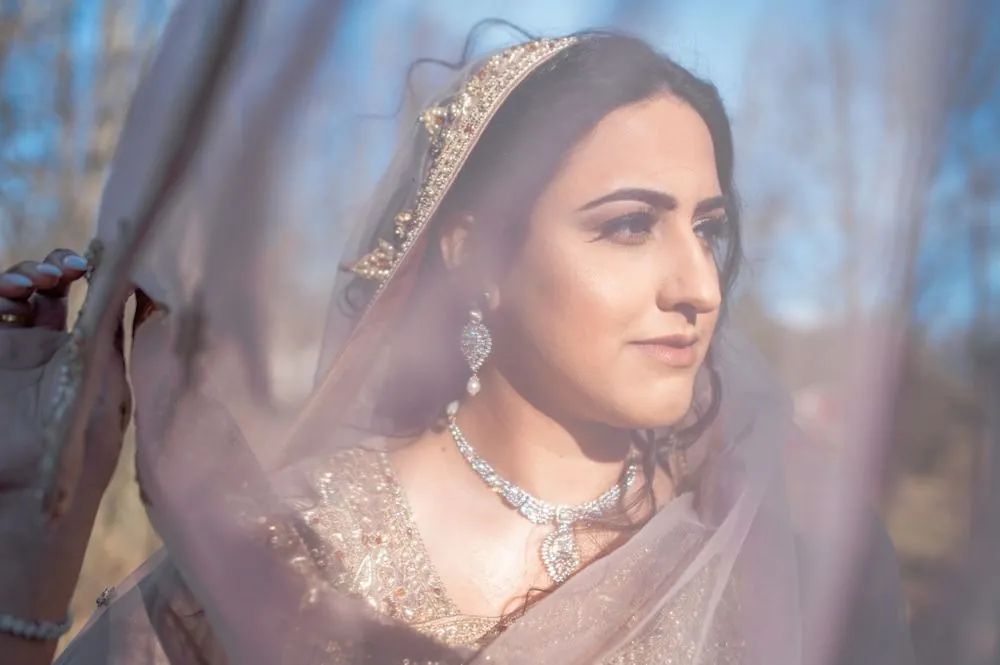 The bride gazes past the camera through a veil of pink chiffon in winter sun