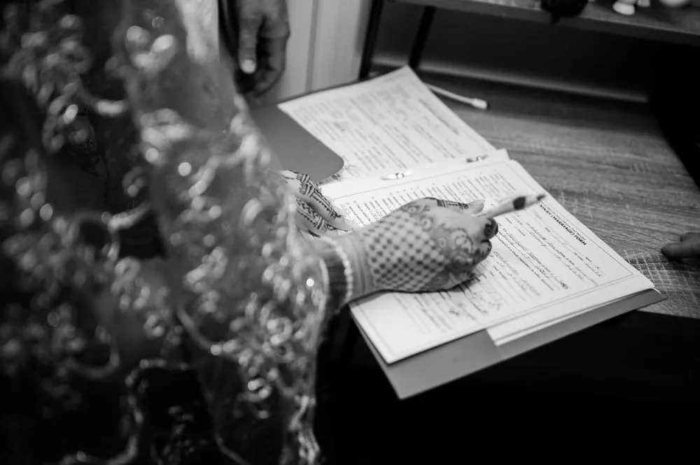 The bride's hennaed hand signs the marriage documents, in black and white