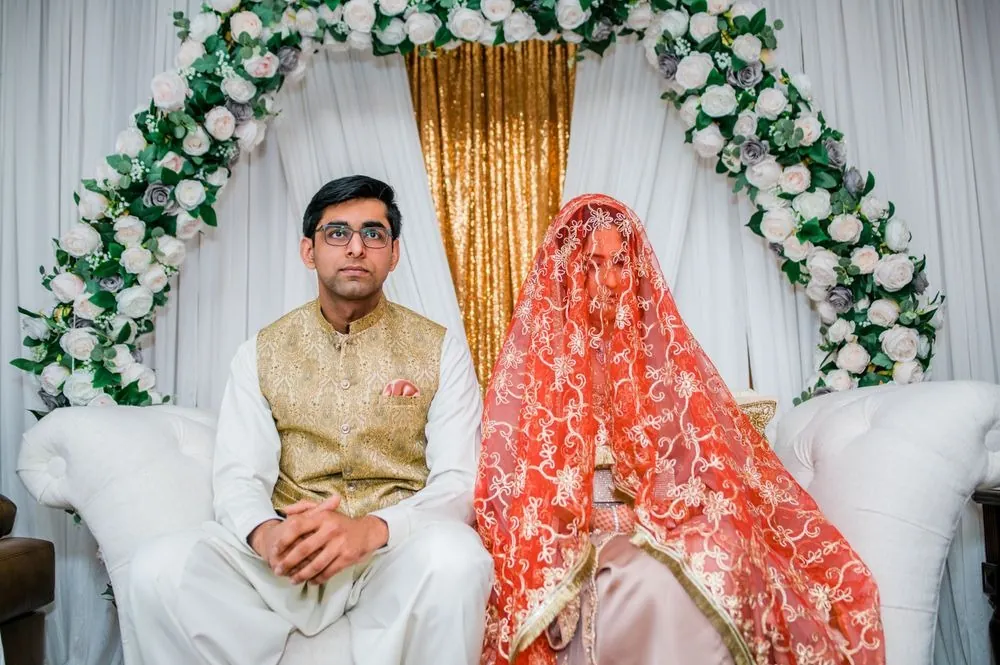 Sohaib and Qaniat sit together under the rose arch, her face covered by the coral veil