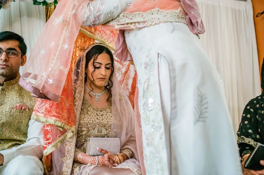 The coral veil is lifted from over the bride as she sits beside the groom