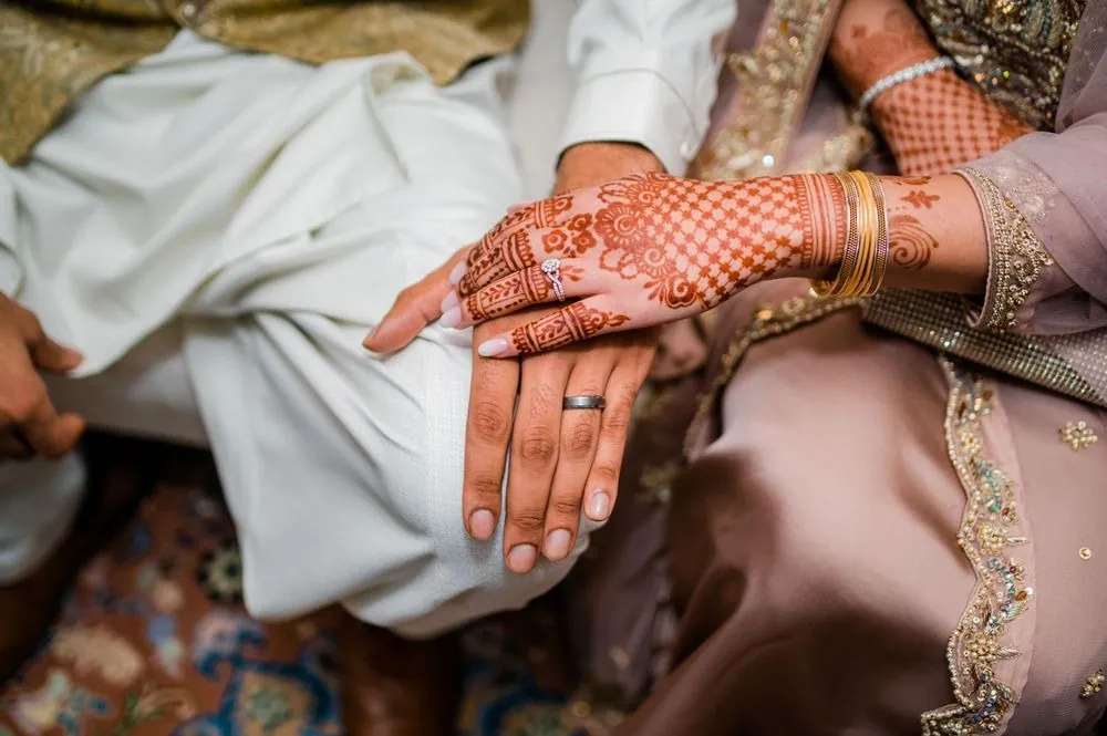 The bride's hennaed hand rests on the groom's hand, a new band on his finger