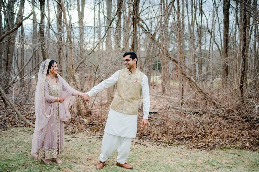 Qaniat and Sohaib hold hands and smile at each other at the edge of bare woods