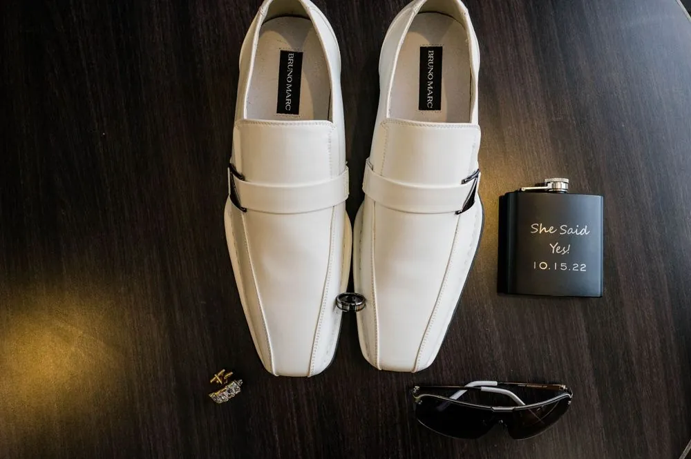 White loafers, cufflinks and a small black flask laid out on a dark floor
