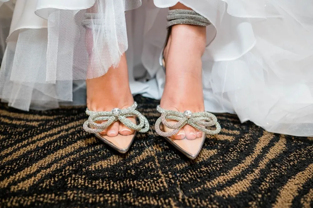 Jeweled bow heels peek out from under layers of white tulle on a patterned carpet