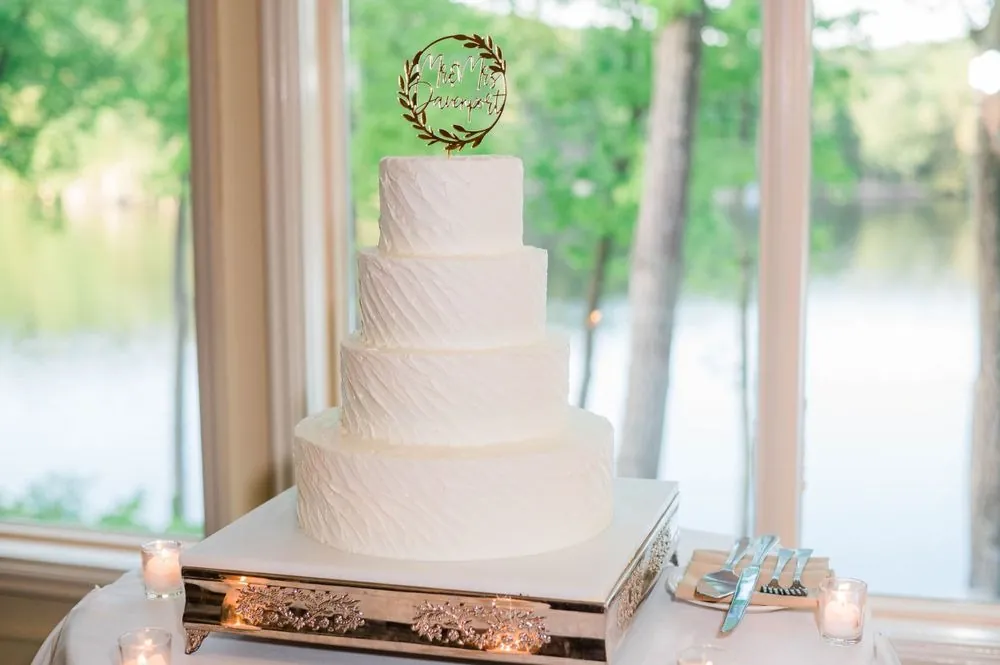 A tiered white cake stands in front of tall windows looking out over the water
