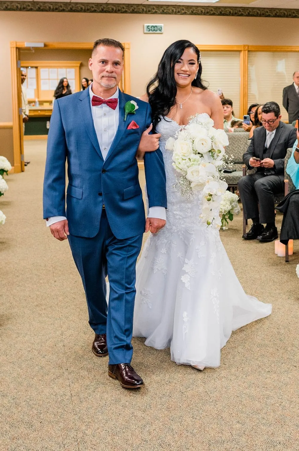 The bride walks down the aisle on the arm of a man in a blue suit
