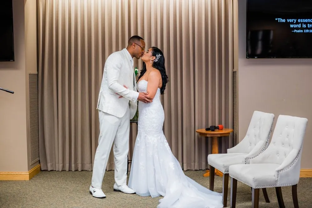 Sollisa and DJ share their first kiss beside a pair of tufted white chairs