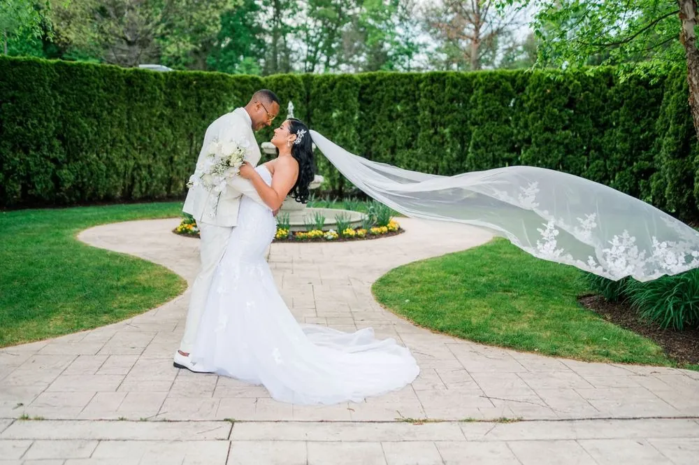 Sollisa and DJ lean in beside a garden fountain as her lace veil streams sideways in the breeze