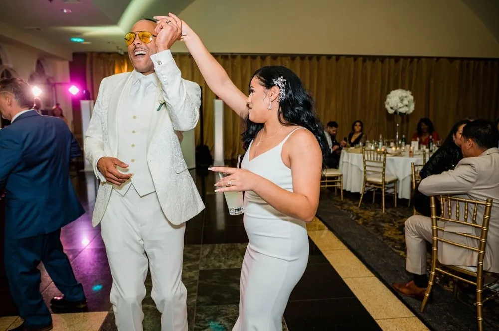 DJ raises one arm mid-dance as Sollisa laughs beside him under purple uplighting