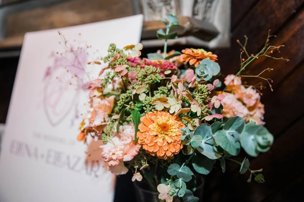 Peach zinnias, blush carnations, and eucalyptus in front of a welcome sign