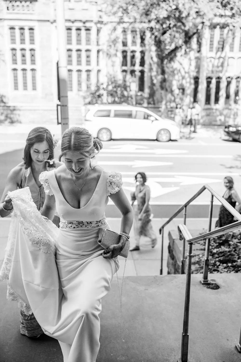 The bride climbs stone steps toward the chapel with a friend, in black and white