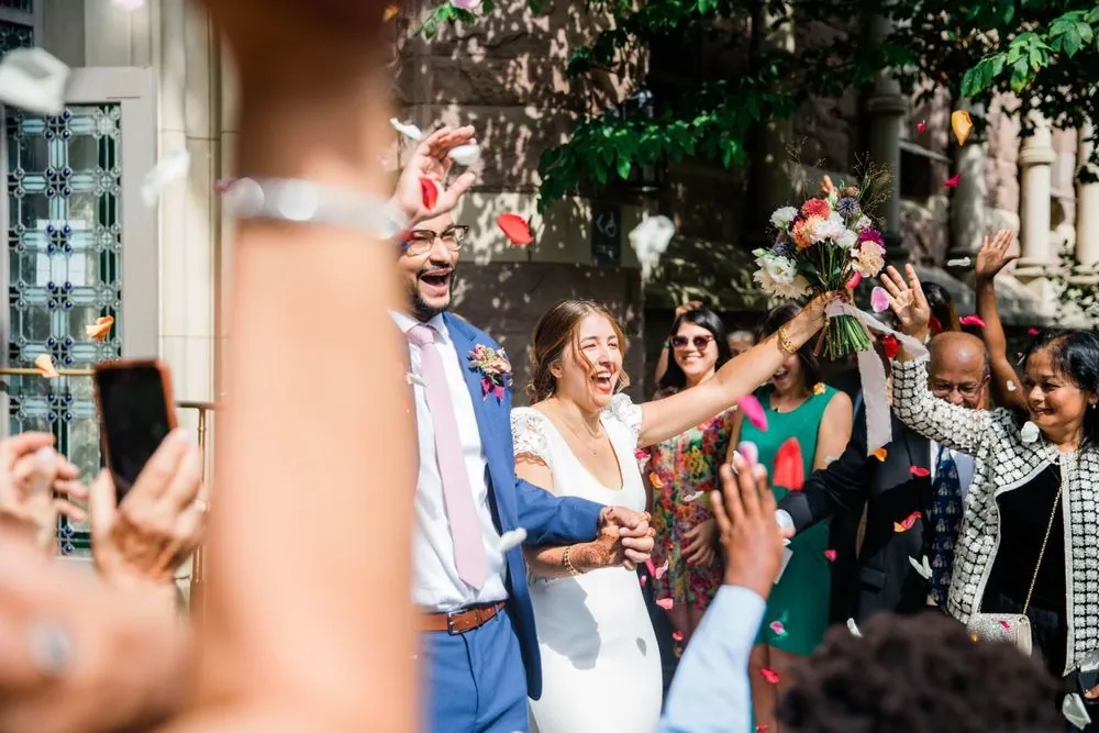 Guests throw petals as the couple leave the chapel laughing