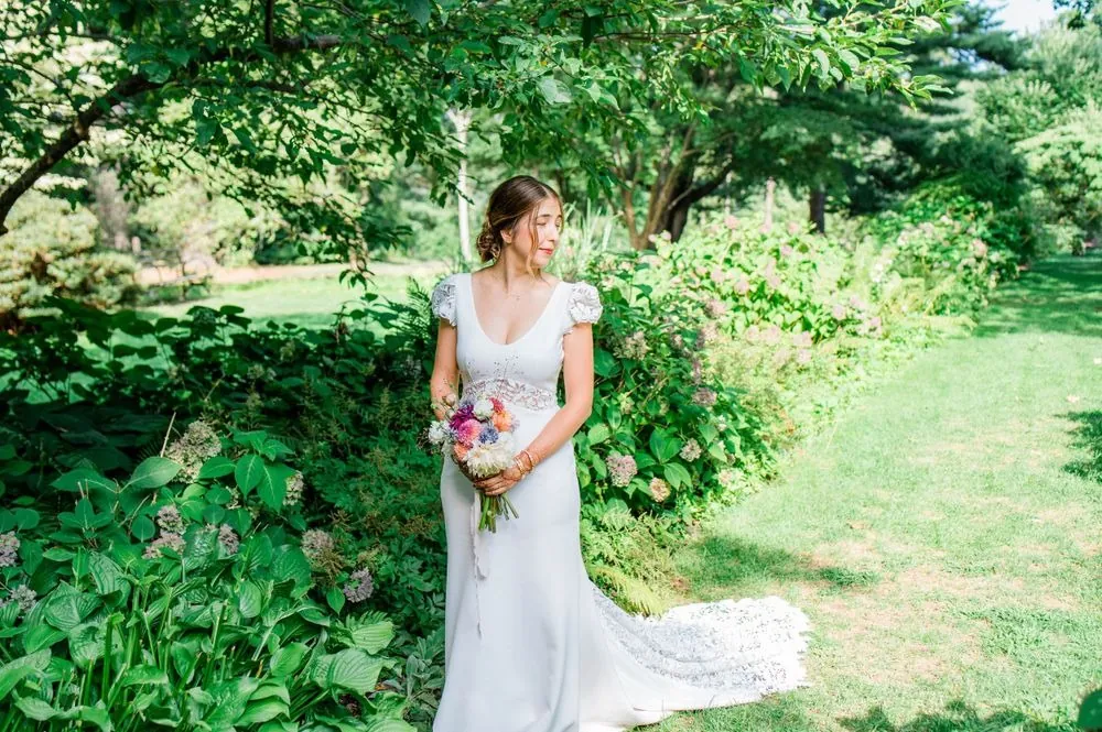 The bride holds a bright bouquet among tall garden plants in Edgerton Park