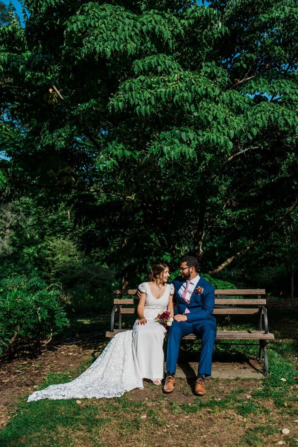 The couple sit on a park bench beneath tall trees in Edgerton Park