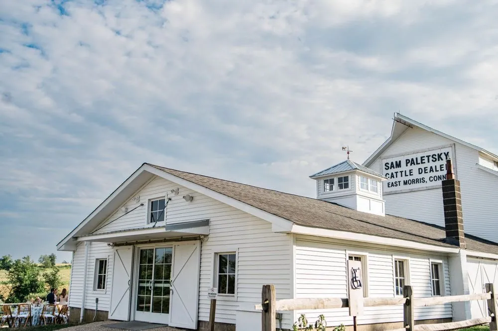 A white barn with a cupola and an old painted sign under summer clouds