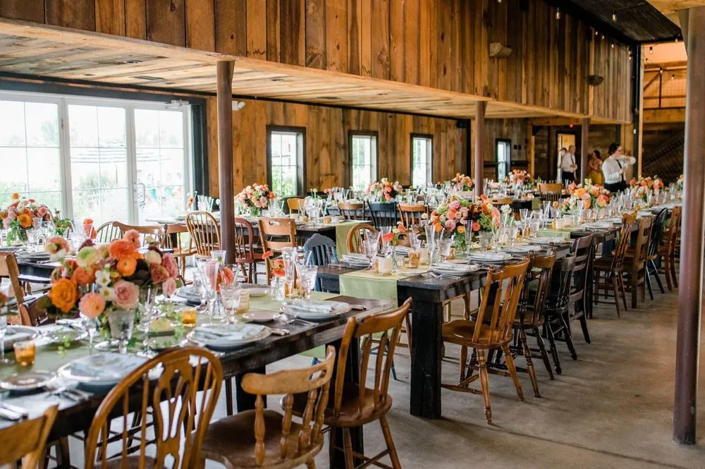 Long wooden tables with orange and blush florals fill the bright barn