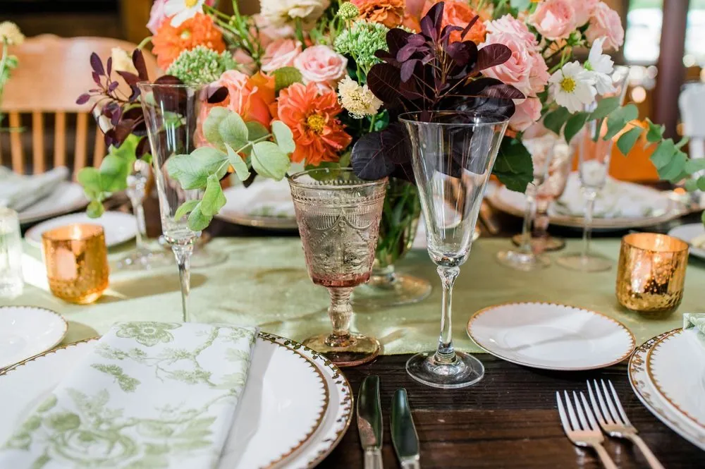 Orange dahlias, amber votives, and etched glassware on a green table runner